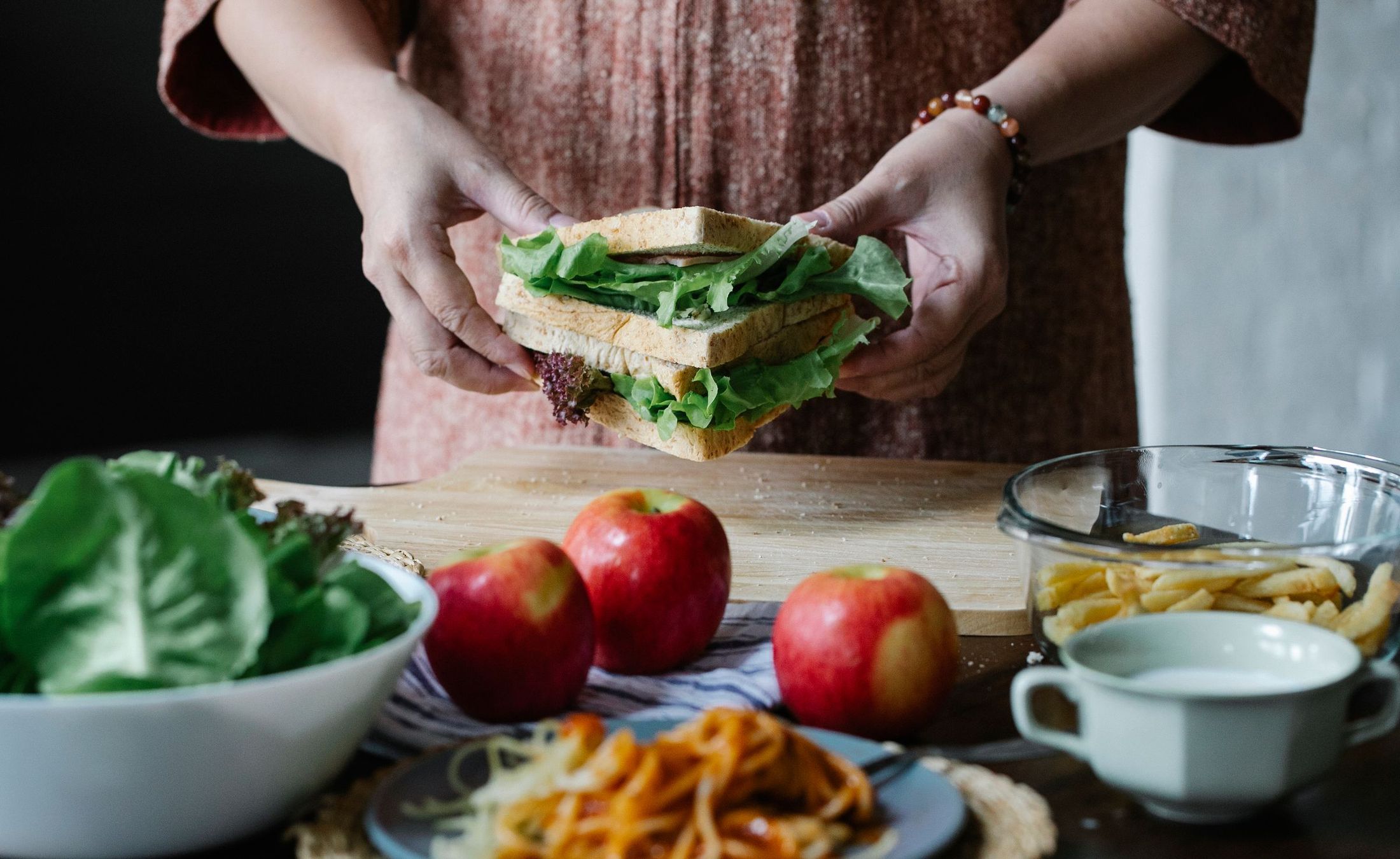 Hands assembling a fresh sandwich with lettuce at a kitchen counter
